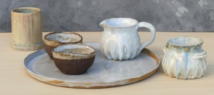 Conjunto de cerámica artesanal con bandeja, cuencos, jarra y vasos decorativos en tonos naturales.