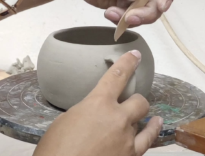 Manos trabajando detalle en taza de barro en proceso de modelado manual